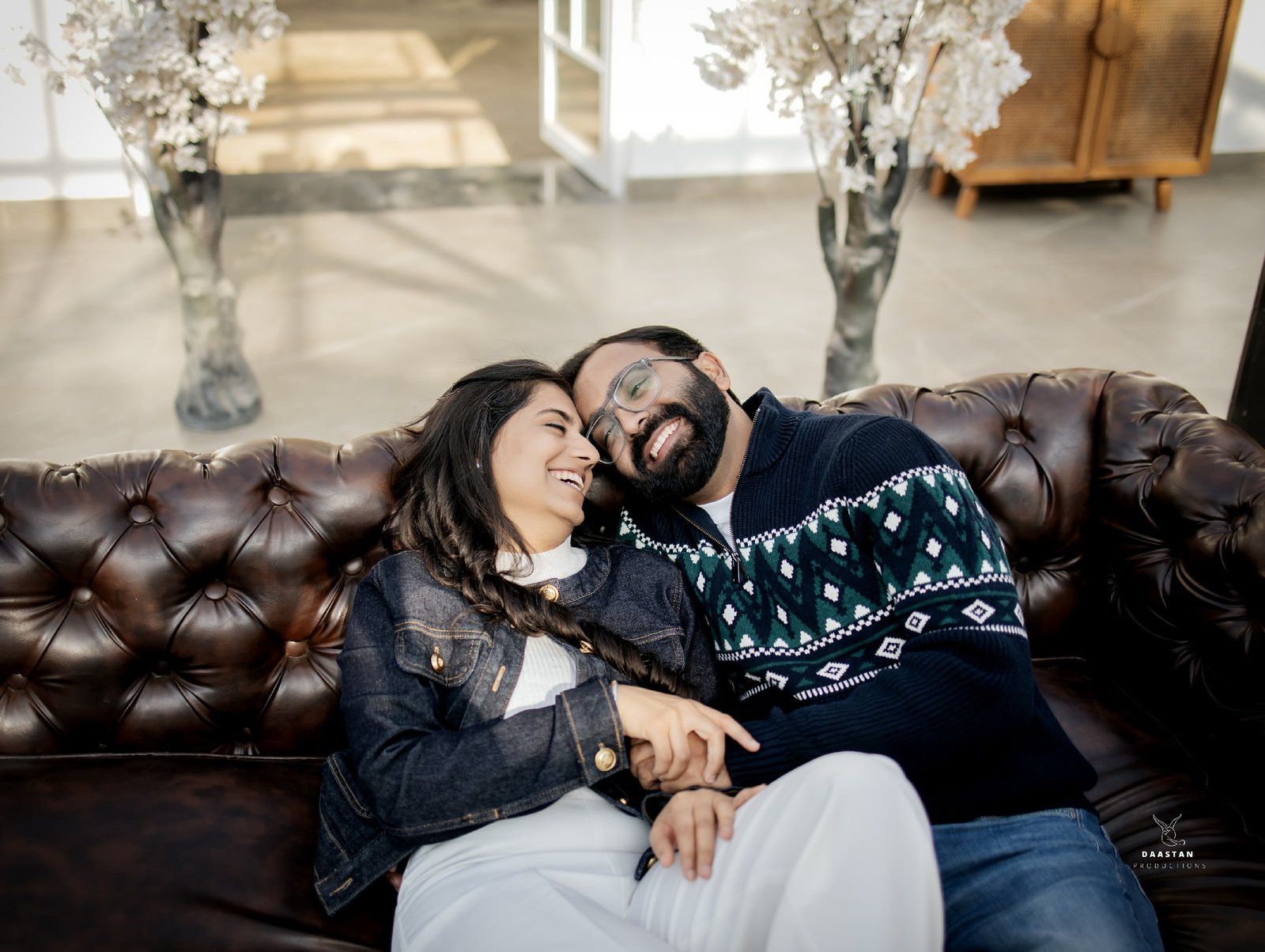 Couple sitting on leather couch in stylish indoor pre-wedding shoot, Indian production house photography