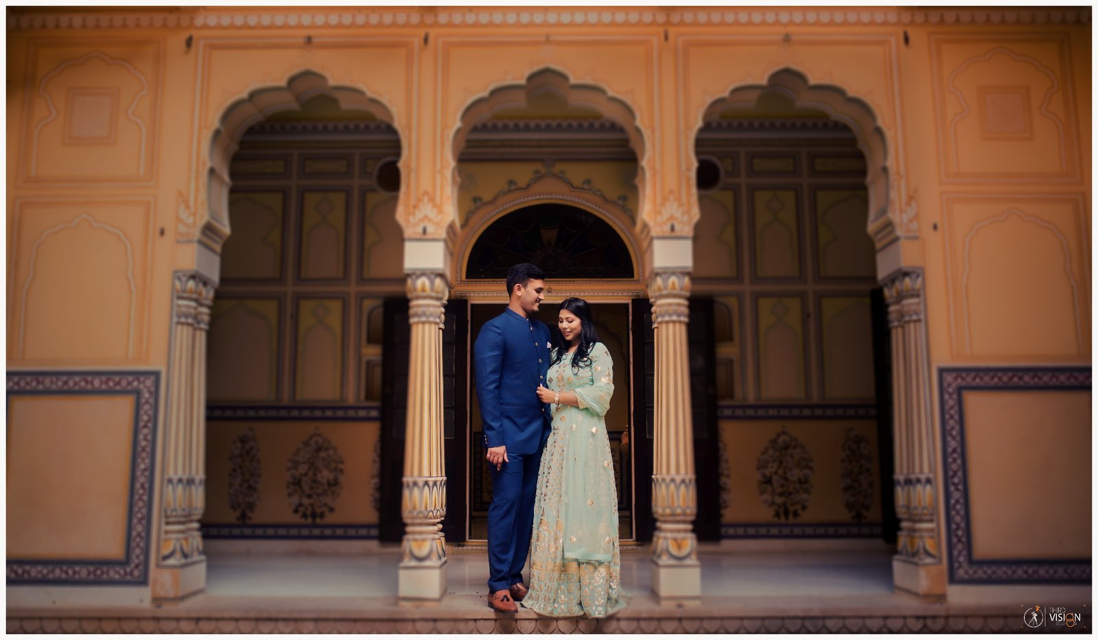 Couple at Rajasthan palace arch in traditional outfits, pre-wedding photography Indian production house
