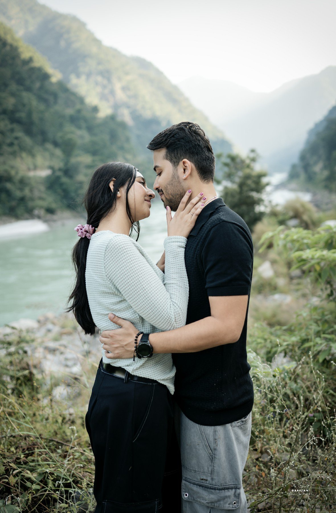 Couple sharing a kiss by riverside mountains during pre-wedding shoot, romantic Indian photography