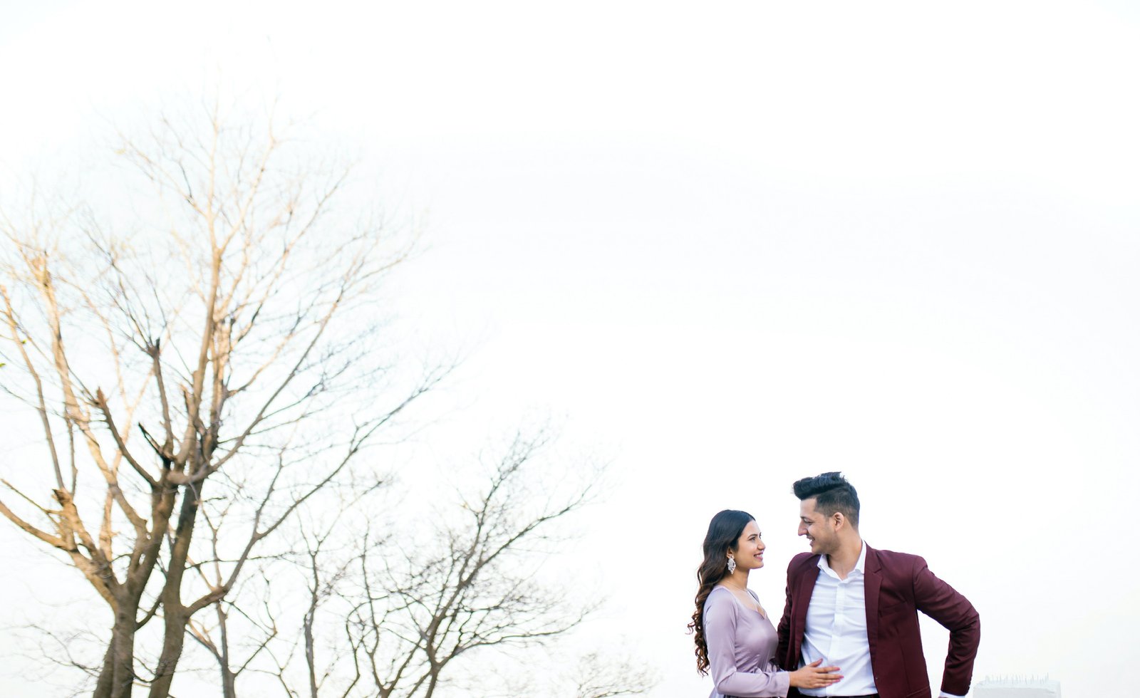Couple near bare winter trees during outdoor pre-wedding shoot, Indian couple photography